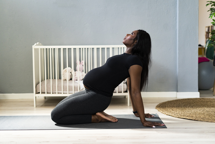 Pregnant young woman leaning back while practicing yoga at home