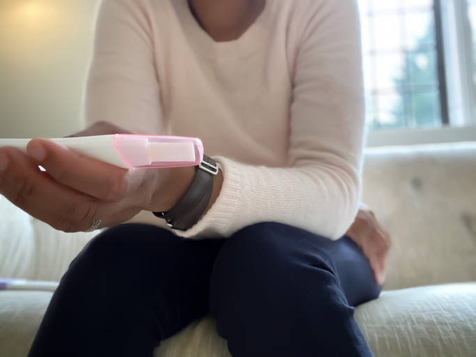 african-american woman reads results of home pregnancy test with second test beside her on couch