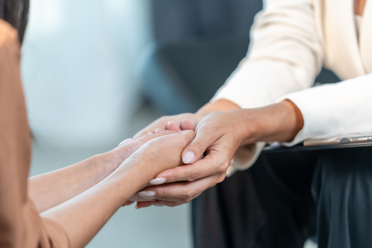 Close up of a female psychologist holding woman's hands during a therapy session. Psychotherapist supporting her depressed patient.