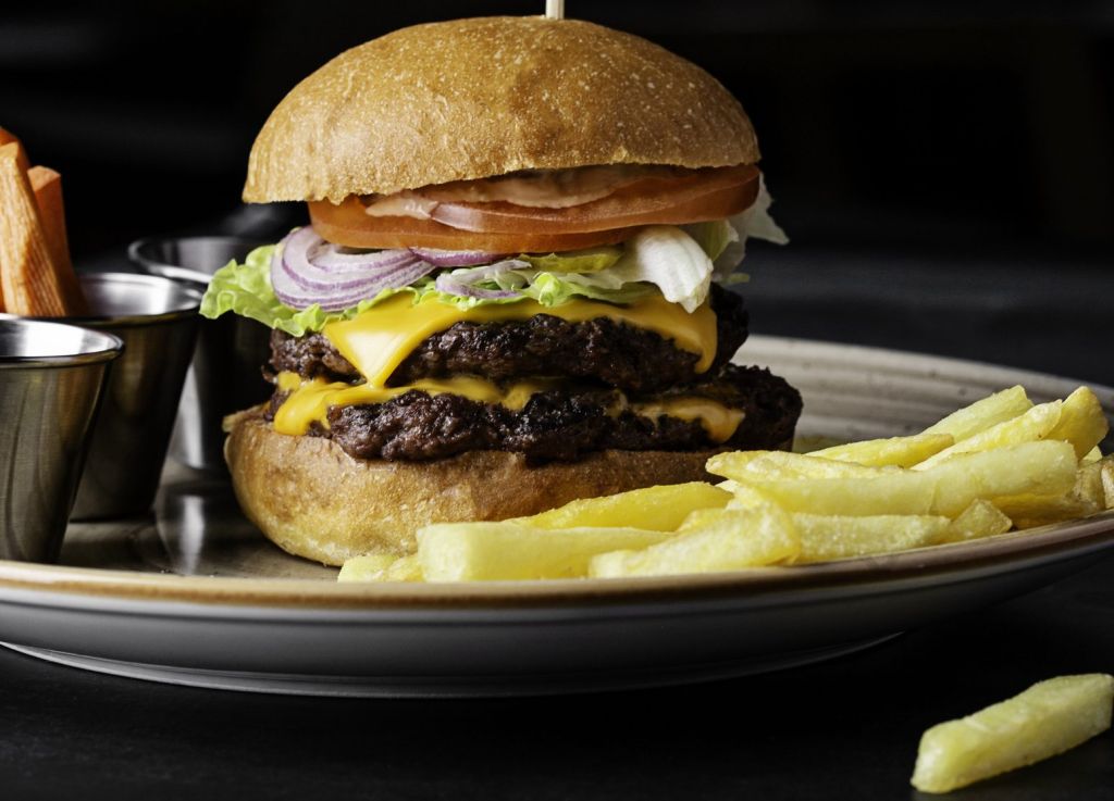 Juicy Double Beef Burger with Caramelized Onions and Fries on Dark Background