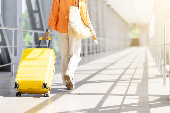 Rear view of black woman walking with suitcase and documents at airport